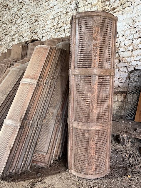 Formelement aus Schichtholz im Lager: einzelne stehende Röhre aus zusammengesetzten Elementen, dahinter einzelne Elemente an weiße Backsteinwand gelehnt